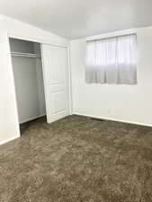 Unfurnished bedroom with a closet, visible vents, dark colored carpet, and baseboards