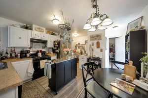 Kitchen featuring black range, light wood-style floors, an inviting chandelier, light countertops, and under cabinet range hood