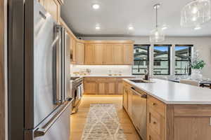 Kitchen with a sink, light countertops, high quality appliances, light wood finished floors, and light brown cabinets