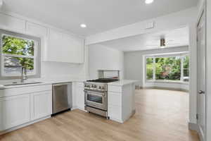 Kitchen with stainless steel appliances, a sink, light countertops, light wood-type flooring, and white cabinets