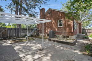Back of property featuring central air condition unit, a chimney, a pergola, brick siding, and a patio area