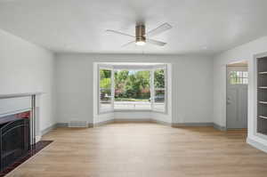 Unfurnished living room featuring ceiling fan, a fireplace with flush hearth, light wood finished floors, and baseboards