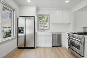 Kitchen featuring appliances with stainless steel finishes, a sink, light wood-style flooring, white cabinets, and light countertops