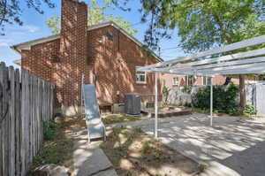 Back of house featuring central AC unit, a chimney, brick siding, and a patio area