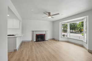 Unfurnished living room featuring light wood-style floors, a ceiling fan, a fireplace with flush hearth, baseboards, and recessed lighting