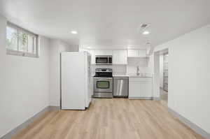 Kitchen featuring stainless steel appliances, a sink, light wood-style flooring, white cabinets, and light countertops