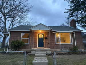 View of front of home with a fenced front yard, a gate, a chimney, brick siding, and a shingled roof