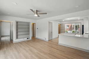 Unfurnished living room featuring built in shelves, a ceiling fan, light wood finished floors, recessed lighting, and baseboards