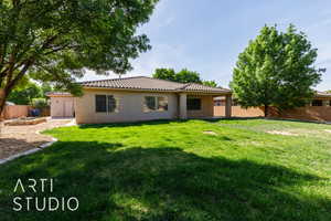 Rear view of house featuring fence, stucco siding, a tiled roof, and a lawn