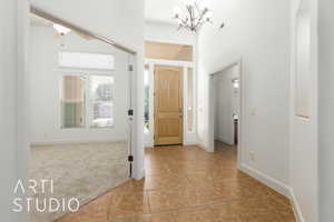 Carpeted foyer entrance with a chandelier, visible vents, tile patterned flooring, and baseboards