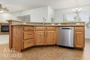 Kitchen featuring a sink, light stone counters, hanging light fixtures, dishwasher, and ceiling fan with notable chandelier
