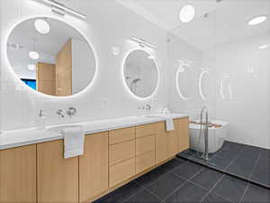 Full bathroom featuring a freestanding tub, double vanity, tile patterned flooring, tile walls, and a sink