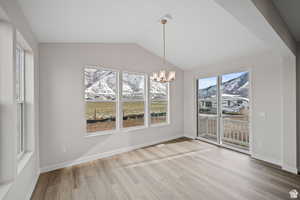 Unfurnished dining area featuring an inviting chandelier, wood finished floors, lofted ceiling, a mountain view, and baseboards
