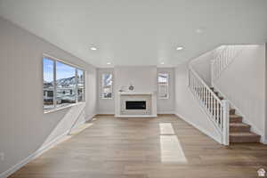 Unfurnished living room featuring baseboards, stairway, a glass covered fireplace, and light wood finished floors
