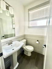 Half bath with toilet, a wainscoted wall, wood finished floors, and a sink