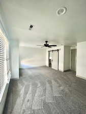 Carpeted spare room featuring a barn door, baseboards, a ceiling fan, and visible vents