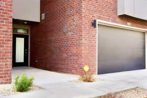 Doorway to property with brick siding, visible vents, and a garage