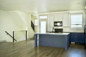 Kitchen featuring tasteful backsplash, an island with sink, dark wood-style floors, and black appliances