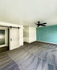 Unfurnished room with a barn door, dark colored carpet, baseboards, and ceiling fan