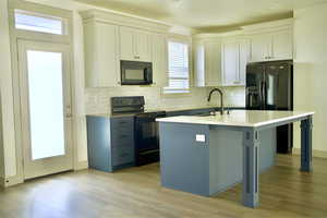 Kitchen featuring light wood finished floors, a sink, backsplash, light countertops, and black appliances