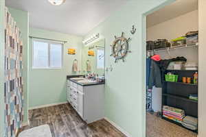 Bathroom featuring wood finished floors, vanity, baseboards, and a walk in closet