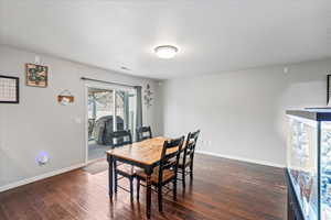 Dining room featuring dark wood-type flooring, visible vents, baseboards, and a textured ceiling