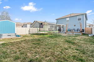 Rear view of house featuring a yard, a trampoline, fence, and a pergola