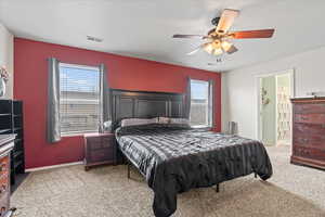 Carpeted bedroom featuring ceiling fan, multiple windows, and visible vents