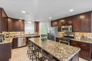 Kitchen with light tile patterned floors, a center island, a sink, appliances with stainless steel finishes, and backsplash