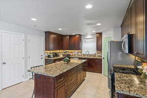 Kitchen with light tile patterned floors, visible vents, a kitchen island, a sink, and stainless steel appliances