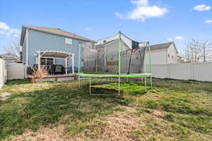 Back of property with a trampoline, a pergola, a fenced backyard, and a lawn