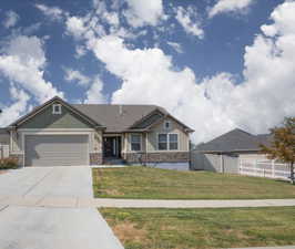Craftsman-style home with concrete driveway, stone siding, a front lawn, a garage, and fence