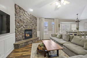 Living room featuring hardwood / wood-style flooring, vaulted ceiling, ceiling fan, and a fireplace