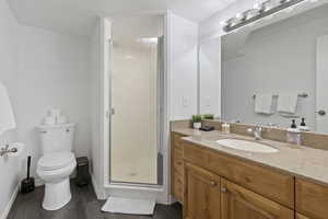 Bathroom featuring vanity, hardwood / wood-style floors, a shower with door, and toilet
