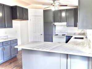 Kitchen featuring a peninsula, electric range, a ceiling fan, under cabinet range hood, and a sink