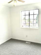 Carpeted empty room featuring visible vents, ceiling fan, and baseboards