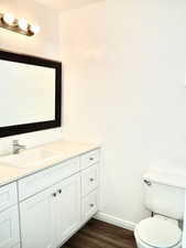 Bathroom with toilet, wood finished floors, vanity, and baseboards