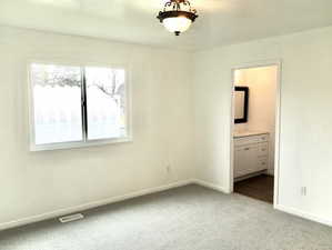 Unfurnished bedroom with visible vents, light colored carpet, baseboards, and connected bathroom