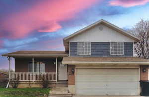 Tri-level home with roof mounted solar panels, a porch, brick siding, a garage, and driveway