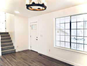 Foyer with a chandelier, stairs, dark wood-style flooring, and baseboards