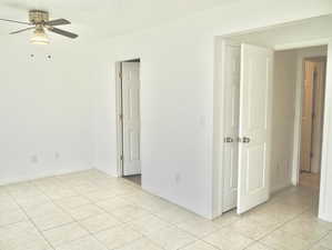 Empty room with light tile patterned floors, baseboards, and a ceiling fan