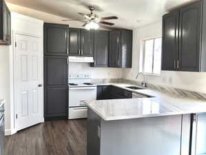 Kitchen with a sink, a ceiling fan, a peninsula, under cabinet range hood, and white electric range oven