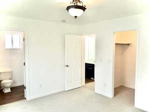 Unfurnished bedroom with a closet, baseboards, a walk in closet, ensuite bath, and light colored carpet