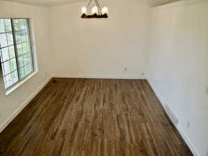 Unfurnished dining area with visible vents, a notable chandelier, dark wood finished floors, and baseboards
