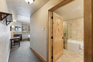 Hall with light tile patterned floors, a textured ceiling, and baseboards