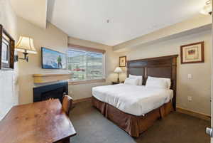 Carpeted bedroom with a lit fireplace and baseboards