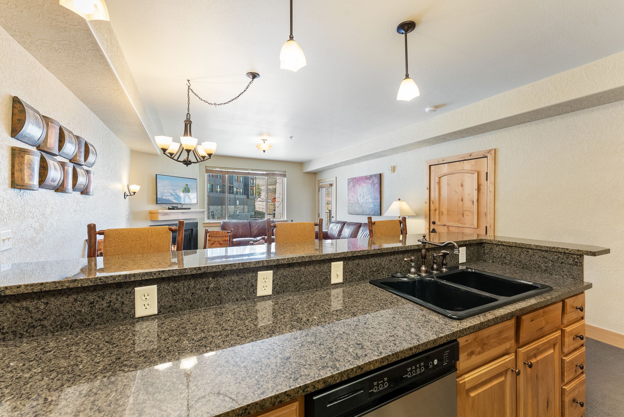 Kitchen peninsula featuring a double basin sink with a bronze-finish faucet, granite-finish countertops, and wood-finish cabinetry