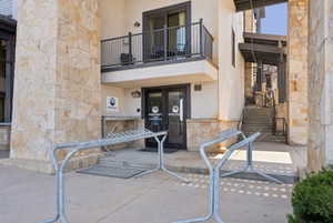 View of exterior entry with stucco siding, stone siding, and a balcony