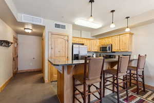 Kitchen featuring a kitchen bar, light brown cabinetry, visible vents, stainless steel appliances, and baseboards