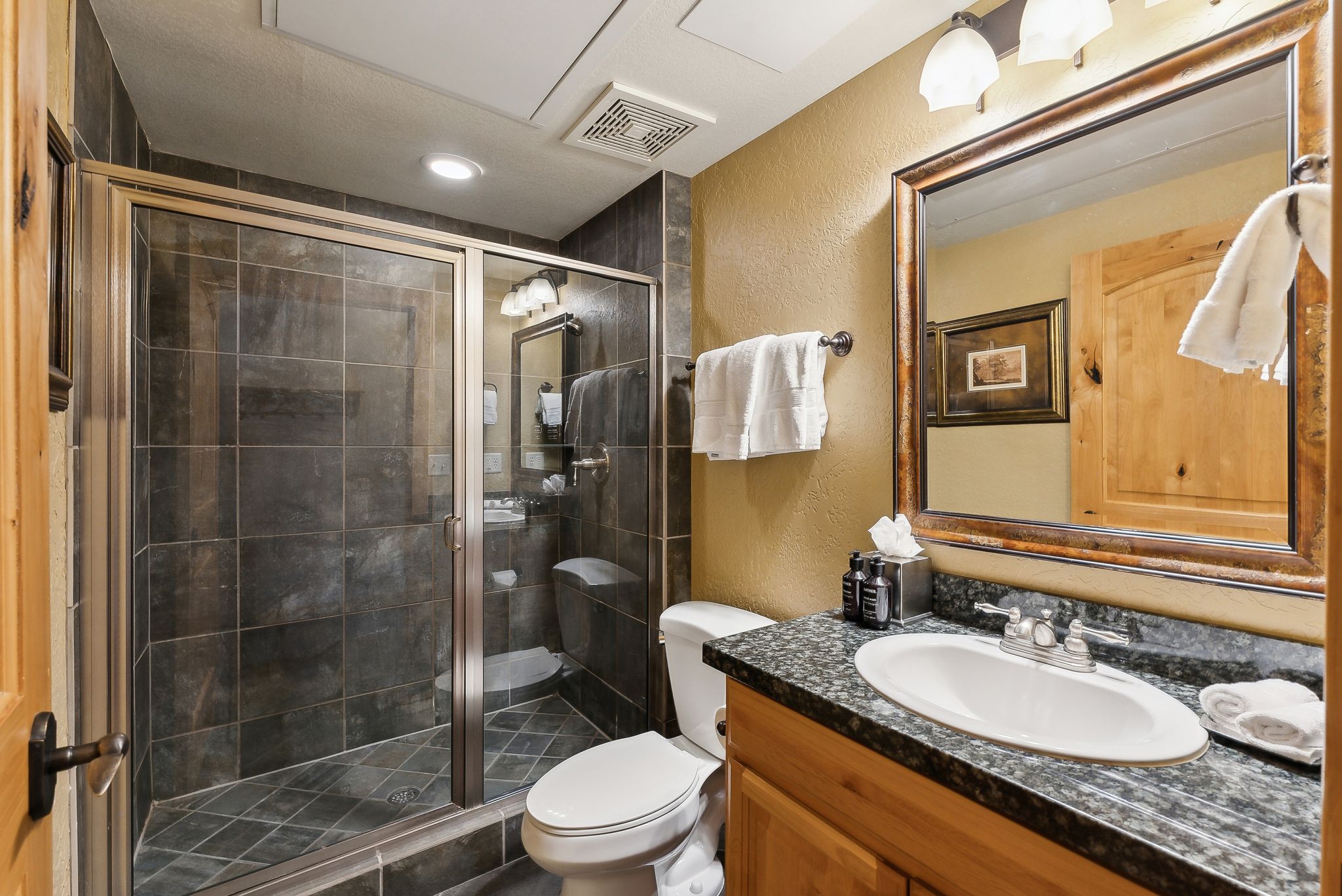 Full bathroom featuring a glass-enclosed shower with dark tile surround, a granite-finish countertop vanity with an undermount sink, and a framed mirror